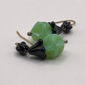 May include: A pair of dangle earrings with green glass beads and black glass flower accents.