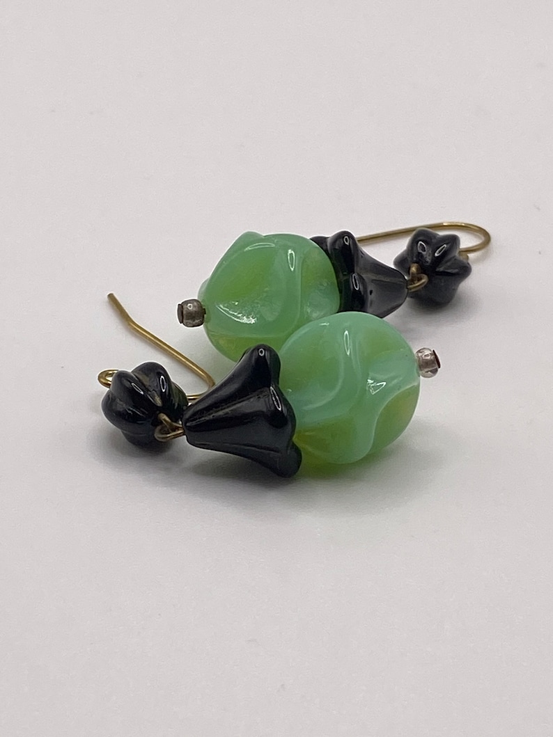 May include: A pair of dangle earrings with green glass beads and black glass flower accents.