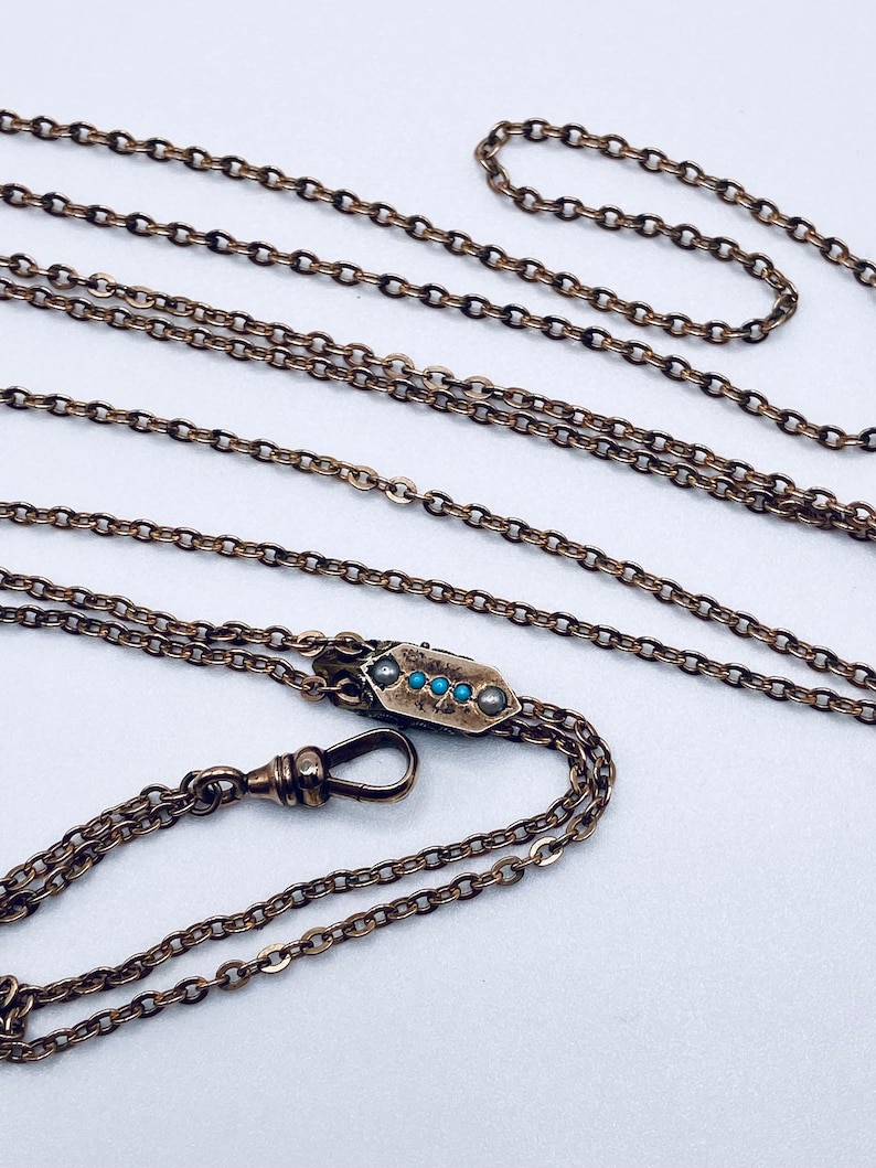 May include: A gold chain with a decorative clasp featuring blue and white stones. The chain is made of linked circles and has a hook on one end.