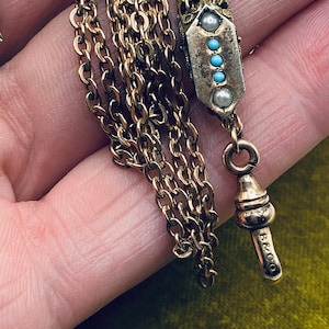 May include: A gold chain with a decorative pendant featuring turquoise and pearl accents. The chain has a fob with the inscription "B & CO."