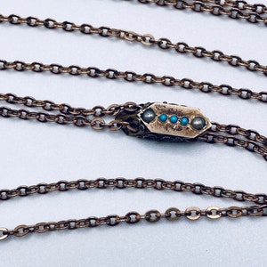 May include: A gold chain necklace with a pendant featuring a small, rectangular design with five turquoise stones.