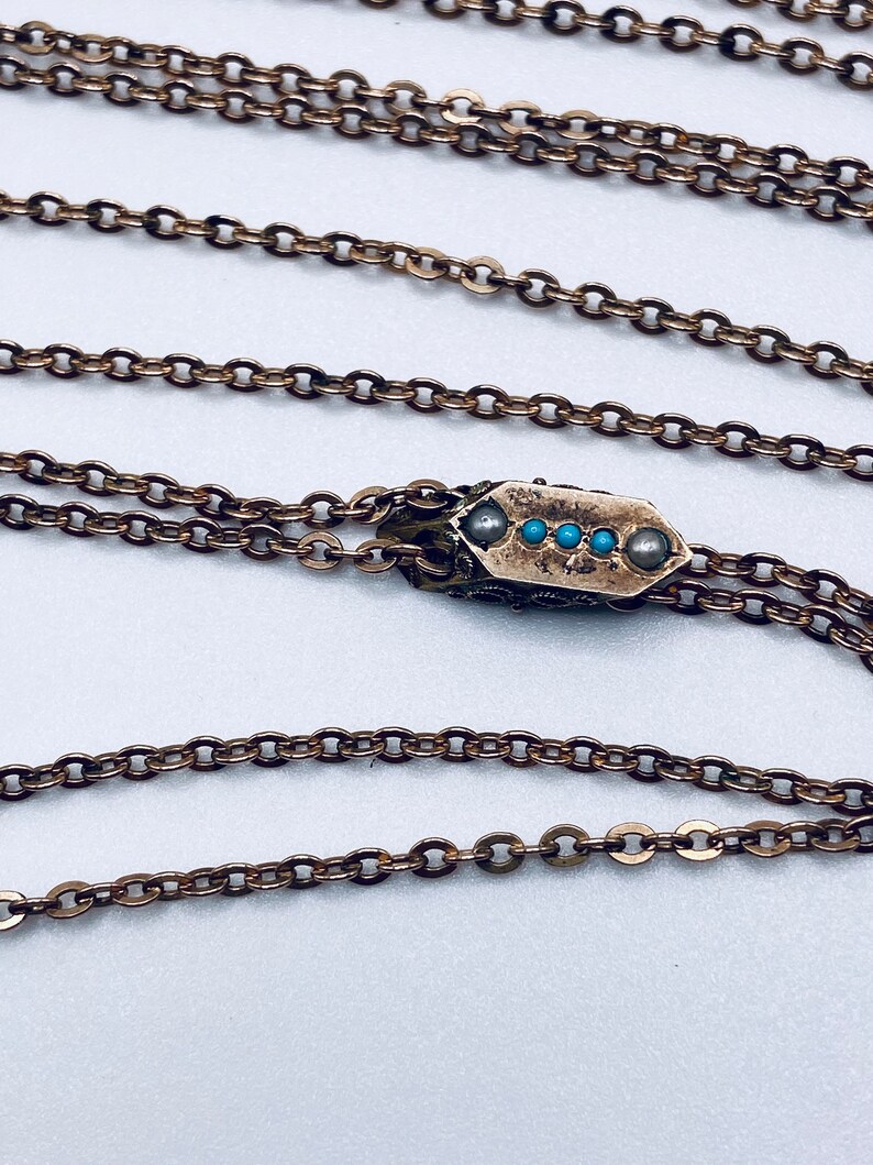 May include: A gold chain necklace with a pendant featuring a small, rectangular design with five turquoise stones.