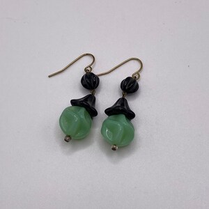 May include: A pair of dangle earrings with green and black glass beads. The earrings have gold hooks.