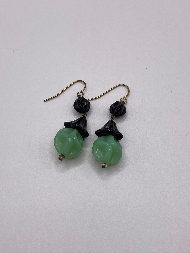 May include: A pair of dangle earrings with green and black glass beads. The earrings have gold hooks.