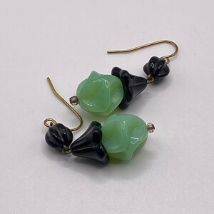 May include: A pair of earrings with green and black glass beads. The beads are shaped like flowers and are attached to gold-colored hooks.