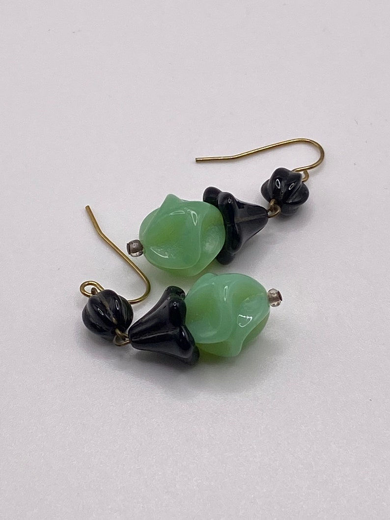 May include: A pair of earrings with green and black glass beads. The beads are shaped like flowers and are attached to gold-colored hooks.