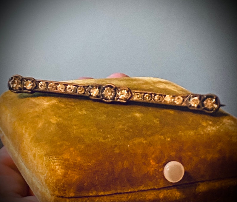 May include: A vintage silver bar pin with a row of clear rhinestones set in a geometric pattern.
