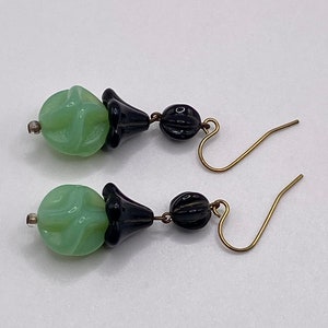 May include: A pair of dangle earrings with green and black glass beads. The green beads are swirled and the black beads are smooth. The earrings have gold hooks.