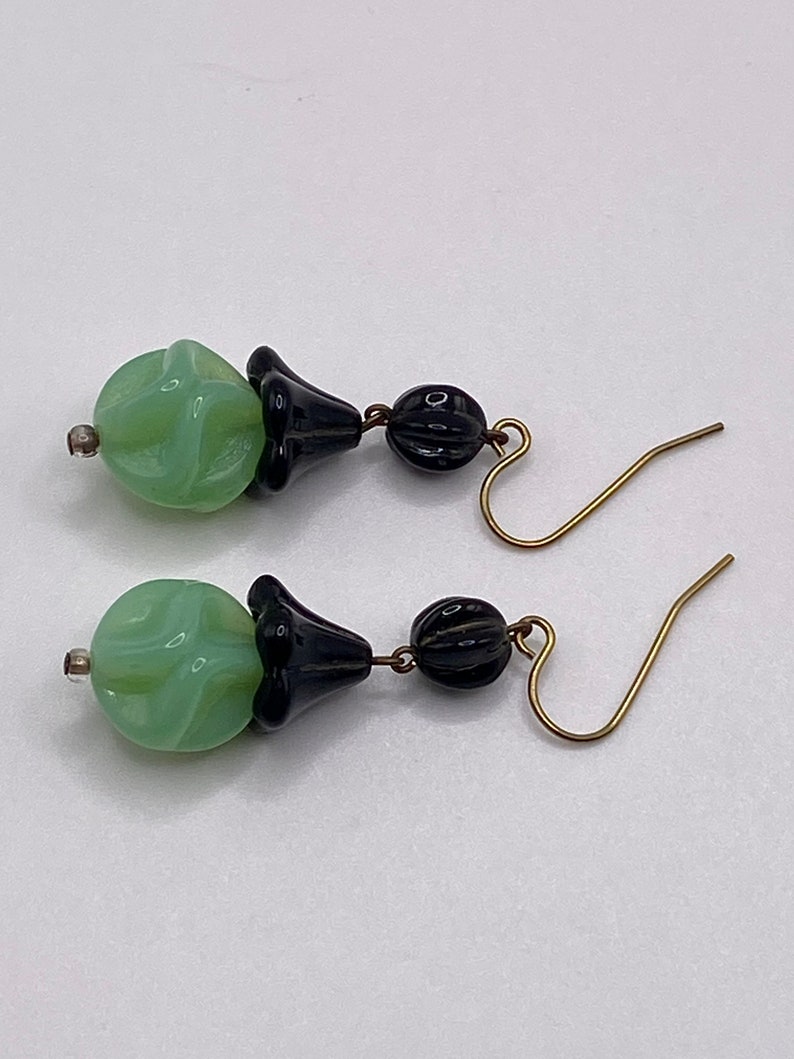 May include: A pair of dangle earrings with green and black glass beads. The green beads are swirled and the black beads are smooth. The earrings have gold hooks.
