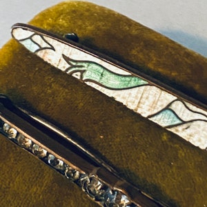 May include: Two vintage hair clips, one with a green and white enamel design and the other with a row of clear rhinestones.