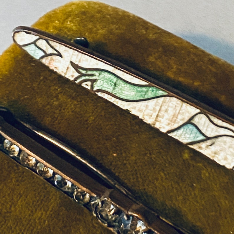 May include: Two vintage hair clips, one with a green and white enamel design and the other with a row of clear rhinestones.