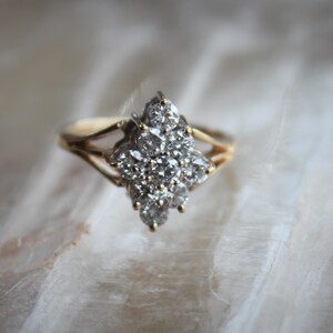 May include: A gold ring with a cluster of small, clear diamonds set in a flower-like design.