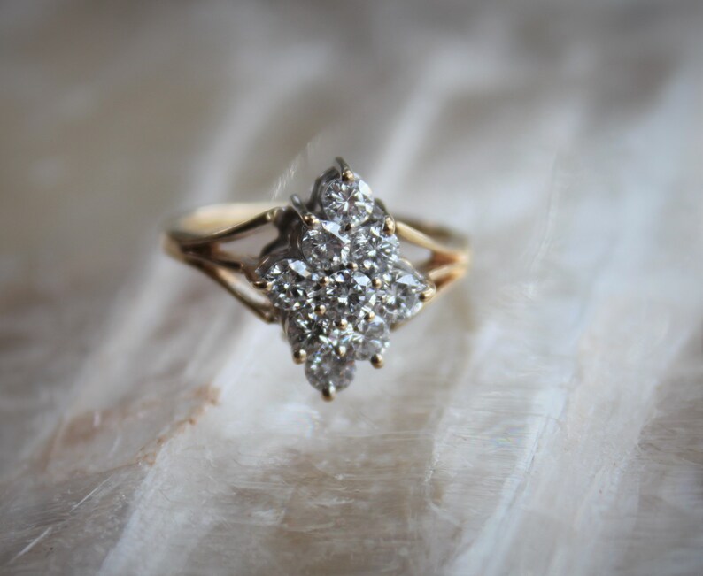 May include: A gold ring with a cluster of small, clear diamonds set in a flower-like design.
