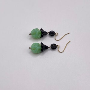 May include: A pair of dangle earrings with green and black glass beads. The beads are carved with a floral design. The earrings have gold-toned hooks.