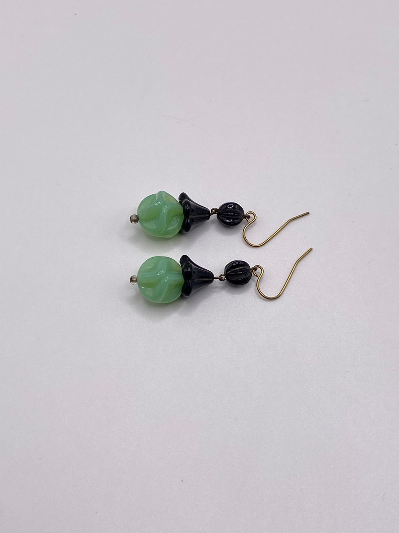 May include: A pair of dangle earrings with green and black glass beads. The beads are carved with a floral design. The earrings have gold-toned hooks.