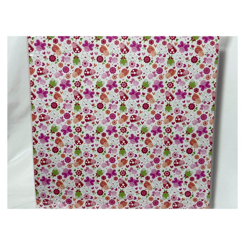 Op de afbeelding: Een rechthoekig vel papier met een herhalend patroon van kleine cartoon lieveheersbeestjes, groene kikkers, roze vlinders, oranje slakken, witte enveloppen en donkerroze bloemen op een witte achtergrond met verspreide rode en roze hartjes.