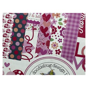 Op de afbeelding: Een collectie van bedrukt knutselpapier met lieveheersbeestjes, stippen, hartjes, bloemen en vichy-ruitjes in tinten roze, rood en wit. Het papier bevat teksten zoals U & ME, Love en een Doodlebug Design-logo met een bijtje.