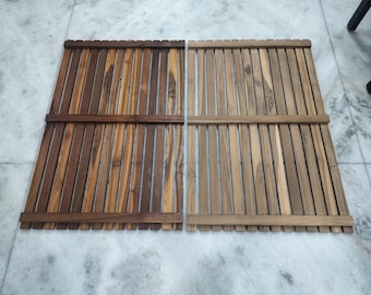 Op de afbeelding: Twee rechthoekige houten matten, elk met verticale lamellen en horizontale steunen. De ene mat is een mix van bruintinten, de andere is lichtbruin. De matten zijn waarschijnlijk voor een badkamer of buitenomgeving.