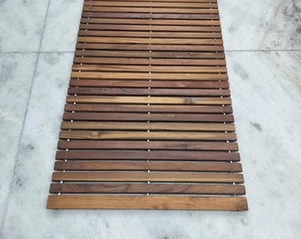 Könnte beinhalten: Ein rechteckiger Badezimmerteppich aus Holz mit horizontalen Lamellen in verschiedenen Brauntönen, die durch kleine Metallbefestigungen gehalten werden. Er liegt auf einem hellgrauen und weißen Marmorboden. Maße: ca. 70 cm x 40 cm.