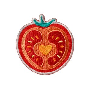 May include: Embroidered patch featuring a cross-section of a tomato. The patch has a red outer edge with a white border. The interior of the tomato is red and orange, with a heart-shaped center. The stem is teal.