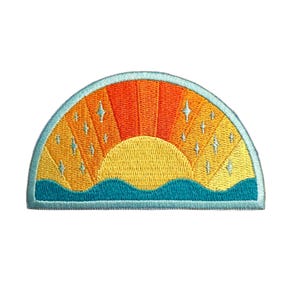 May include: Embroidered patch featuring a stylized sunset design. The patch has a half-circle shape with a gradient of orange, yellow, and blue colors. Small white star shapes are embroidered throughout the design. The bottom edge has a wavy blue line.