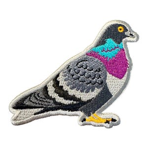 May include: Embroidered patch of a pigeon in profile. The bird features gray, black, teal, purple, and yellow colors. The patch has a white border and is designed to be ironed on or sewn onto fabric. The pigeon is standing.