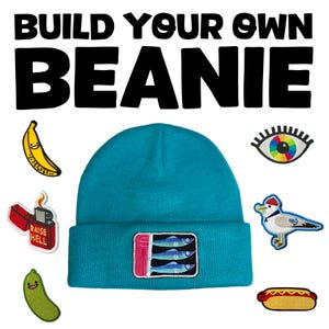 Może przedstawiać: Turkusowa czapka z prostokątną naszywką z trzema rybami. Wokół czapki znajdują się haftowane naszywki z bananem, zapalniczką z napisem "RAISE HELL", ogórkiem, okiem, mewą i hot dogiem. U góry znajduje się napis "BUILD YOUR OWN BEANIE".