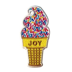 May include: Embroidered patch in the shape of an ice cream cone. The ice cream is white with colorful sprinkles. The cone is yellow with the word "JOY" embroidered on it. The patch has a white border.