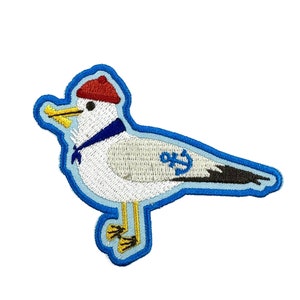 May include: Embroidered iron-on patch of a white seagull wearing a red hat and a blue scarf. The seagull has a yellow beak and black eyes. The seagull has an anchor on its wing. The patch is outlined in blue.