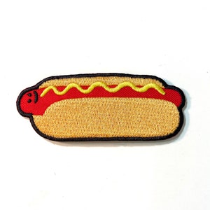 May include: A yellow and red embroidered iron-on patch of a hot dog with mustard. The hot dog has a smiley face.