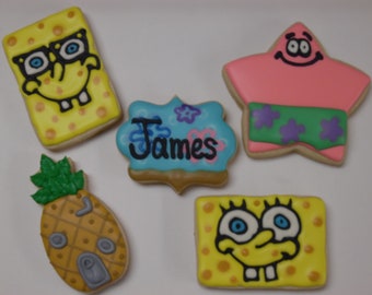 May include: A collection of decorated sugar cookies featuring cartoon characters. Includes a yellow sponge-like character with glasses, a pink starfish, a pineapple, and a cookie with the name "James". The cookies are decorated with colorful icing.
