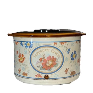 May include: A vintage potpourri crock with a cream-colored base and a brown rim. The crock features a floral design with red, orange, and blue flowers. The words "Potpourri Crock" are printed on the front in a blue oval.