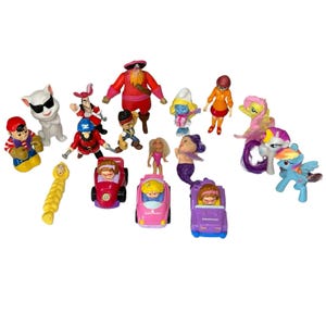 May include: A collection of colorful plastic toy figures, including cartoon characters, dolls, and toy cars. The figures feature a variety of colors and designs, such as a pirate, a Smurf, and My Little Pony figures. The toys are arranged on a white surface.