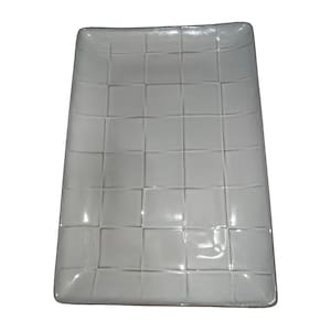 May include: A rectangular white ceramic serving tray featuring a raised grid pattern across its surface. The tray has a glossy finish and slightly rounded corners, with a uniform light gray color throughout the textured square segments.