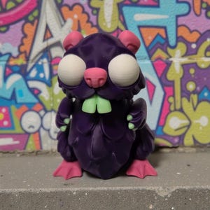 May include: A purple, cartoonish creature with large white eyes, pink ears, nose, and feet, and green teeth. The figure is posed on a gray surface in front of a colorful graffiti background.