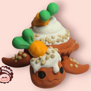 May include: A hand-crafted orange and brown turtle figurine with green leaves and orange carrots on top. The turtle is covered in white frosting and brown sprinkles.