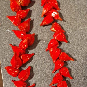 Puede incluir: Una guirnalda roja hecha de pequeños objetos con forma de corazón. La guirnalda está dispuesta en círculo y está sobre una superficie gris.