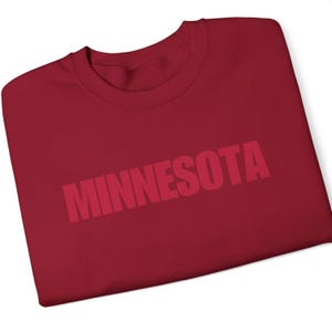 May include: Burgundy red crew neck t-shirt with the word "MINNESOTA" printed in bold, white letters across the front.