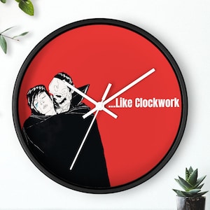 Peut inclure: Une horloge rouge avec des aiguilles noires et un bord noir. Le cadran de l'horloge présente une illustration en noir et blanc de deux personnages avec le texte "...Like Clockwork".
