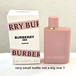 May include: A pink perfume bottle and box set. The box is white with pink text that reads "BURBERRY HER PARFUM". The perfume bottle is a matching pink color with a gold-colored cap. The bottle is 0.16 fl oz.