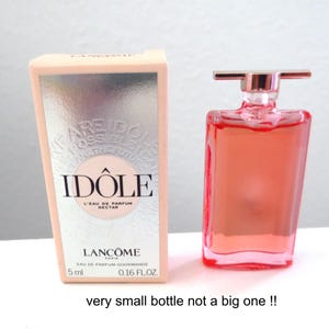 Könnte beinhalten: Ein Miniaturflakon von Lancôme Idôle L'Eau de Parfum Nectar mit rosafarbener Flüssigkeit und einem metallisch silbernen Verschluss, begleitet von der passenden rechteckigen Schachtel. Die Verpackung zeigt den Text Idôle, Lancôme Paris und 5 ml.