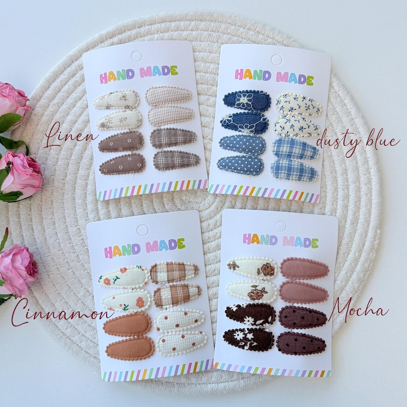 Op de afbeelding: Vier sets met met stof beklede haarspeldjes op witte displaykaarten met het opschrift HAND MADE. Elke kaart bevat acht speldjes met diverse patronen, waaronder ruiten, bloemen, stippen en effen kleuren in verschillende tinten.