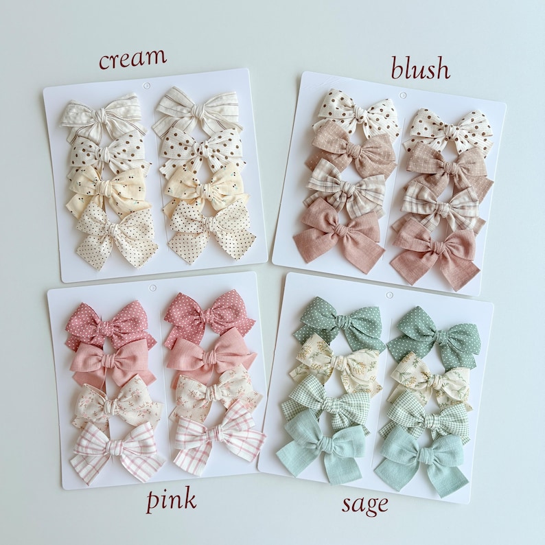 Peut inclure: Quatre cartes de pr&eacute;sentation blanches avec des n&oelig;uds pour cheveux en tissu dans des tons cr&egrave;me, blush, rose et sauge. Chaque carte contient huit n&oelig;uds aux motifs vari&eacute;s, incluant des pois, des rayures et des unis, avec les textes cream, blush, pink, sage.