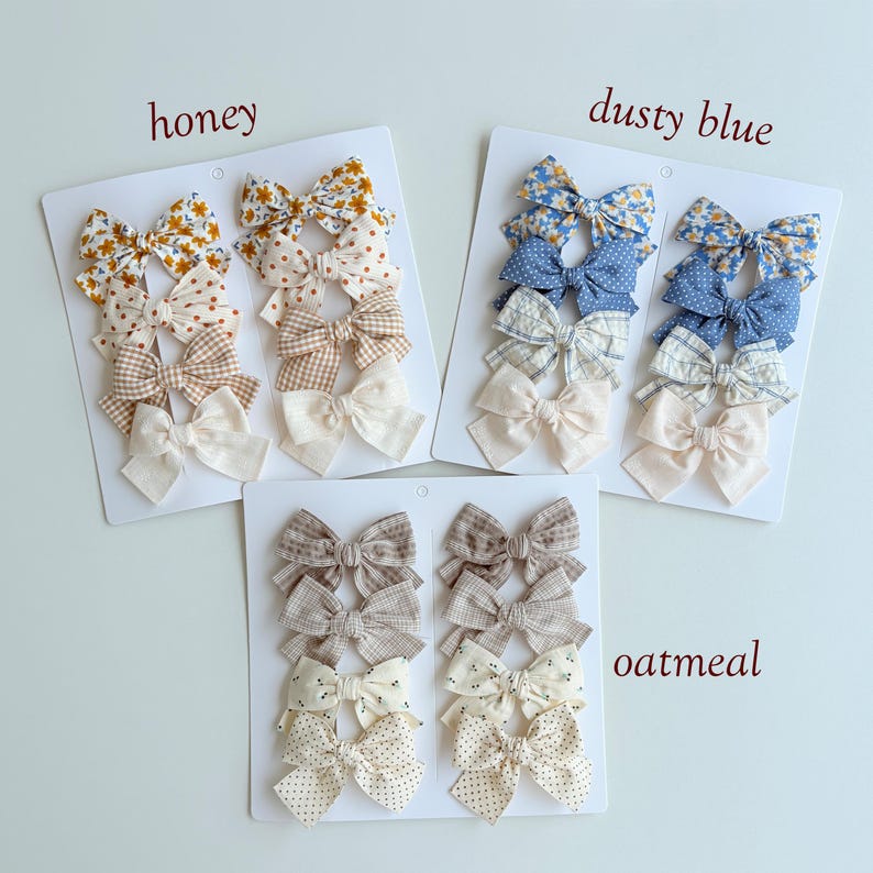 Peut inclure: Trois cartes de pr&eacute;sentation blanches avec des ensembles de n&oelig;uds pour cheveux en tissu. L'ensemble honey pr&eacute;sente des motifs floraux jaunes, &agrave; pois et vichy. L'ensemble dusty blue inclut des motifs floraux bleus, &agrave; pois et &agrave; carreaux. L'ensemble oatmeal montre des motifs &agrave; carreaux et &agrave; pois neutres.