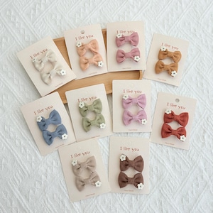 May include: Assortment of hair bows in various colors, including beige, peach, pink, brown, blue, green, purple, and rust. Each bow is paired with a small white flower and displayed on a card that reads "I like you".