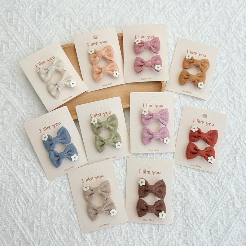 May include: Assortment of hair bows in various colors, including beige, peach, pink, brown, blue, green, purple, and rust. Each bow is paired with a small white flower and displayed on a card that reads "I like you".