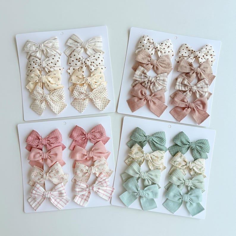 Peut inclure: Quatre cartes de pr&eacute;sentation blanches contenant chacune huit n&oelig;uds pour cheveux en tissu aux motifs et couleurs vari&eacute;s. La collection comprend des tons neutres, roses poudr&eacute;s, vieux rose et vert sauge avec des pois, rayures et carreaux.