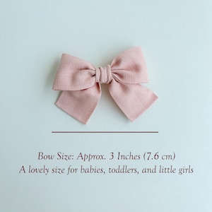 Peut inclure: Un n&oelig;ud pour cheveux en tissu rose poudr&eacute; avec une finition textur&eacute;e. Le n&oelig;ud pr&eacute;sente un n&oelig;ud central et deux boucles sym&eacute;triques. Le texte indique : Bow Size: Approx. 3 Inches (7,6 cm). A lovely size for babies, toddlers, and little girls.