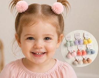 May include: A set of hair ties featuring soft, fuzzy pom-poms in various pastel and neutral colors, including pink, lavender, yellow, mint green, blue, and beige, each attached to a small white display card labeled with the word accessories.