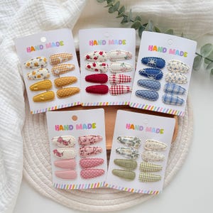 May include: Five white display cards labeled HAND MADE, each holding eight fabric-covered hair clips. The clips feature various patterns including floral, gingham, polka dot, and solid colors in yellow, red, blue, pink, and green palettes.